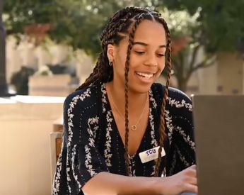 Young woman college student smiling outside while on laptop with TCU badge on.
