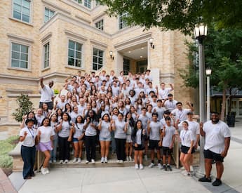 Business Innovation Academy high school students and staff pose on the TCU Neeley School of Business campus, giving the Horned Frogs hand sign