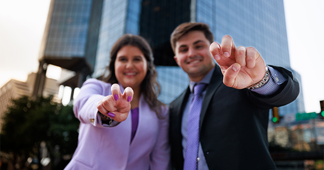 TCU graduates doing the Horned Frog hand sign in downtown Fort Worth