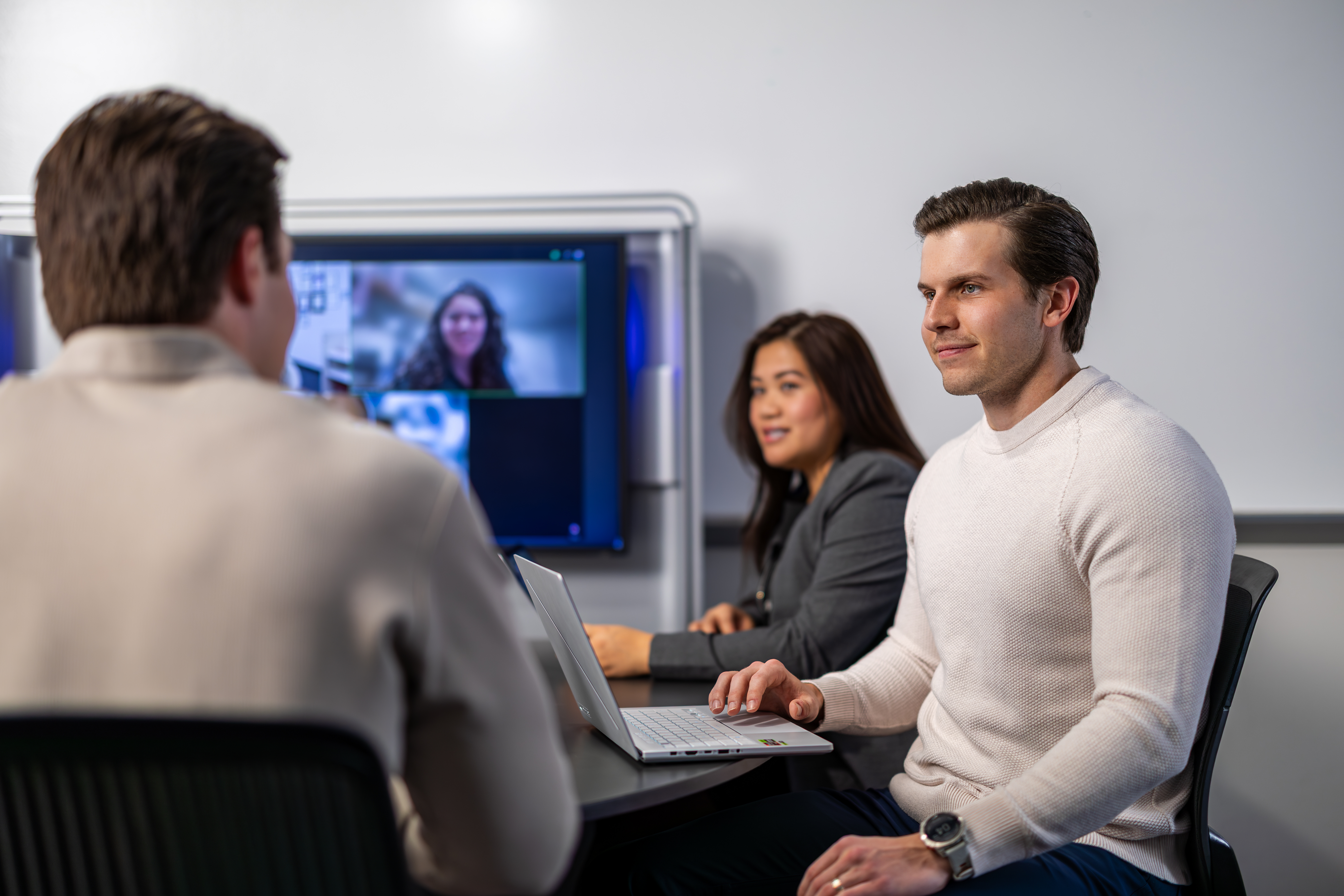 Neeley AI Forward participants collaborate at a laptop during a video call in a modern meeting room