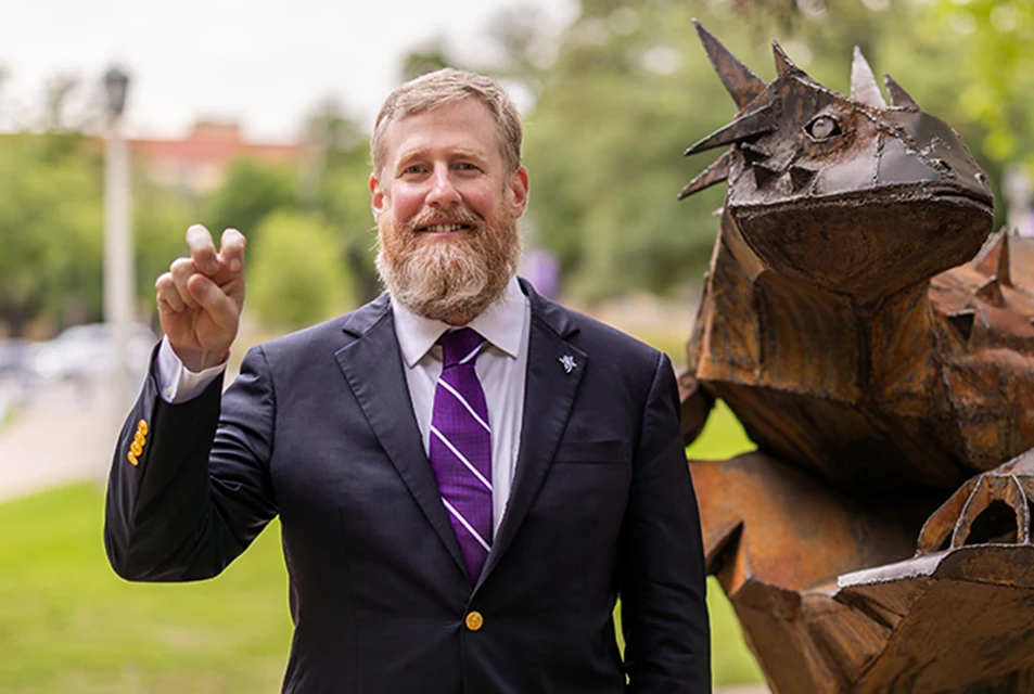 Craig Crossland makes the Go Frogs hand sign while standing next to the iron horned frog statue