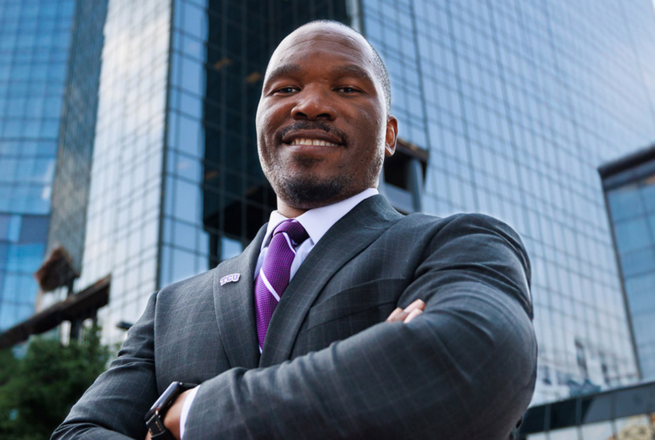 Elijah Clark stands, smiling with arms crossed, in front of a skyscraper