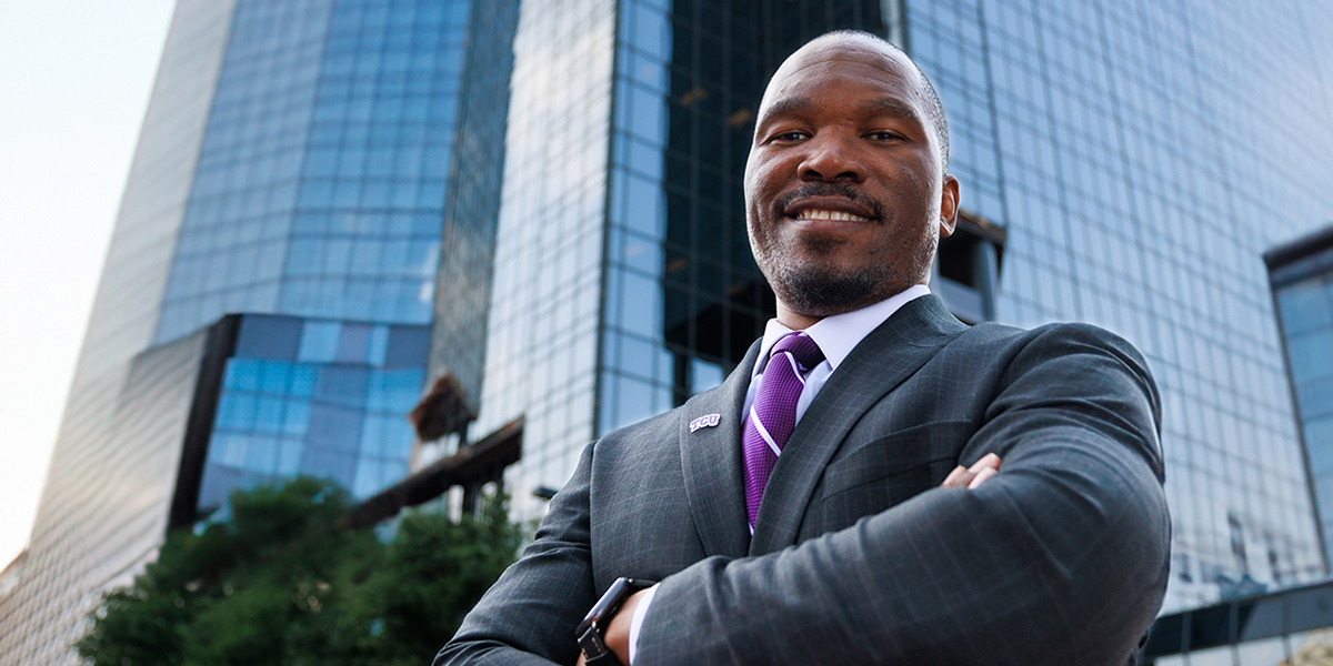 Elijah Clark stands, smiling with arms crossed, in front of a skyscraper