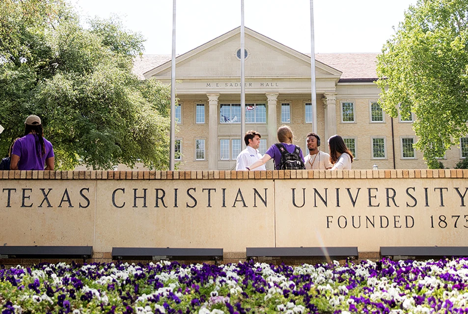 Students gather near the Texas Christian University sign with Sadler Hall in the background