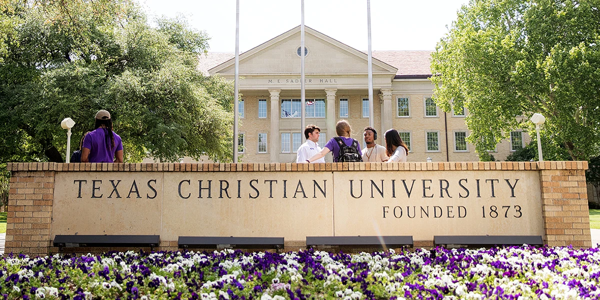 Students gather near the Texas Christian University sign with Sadler Hall in the background