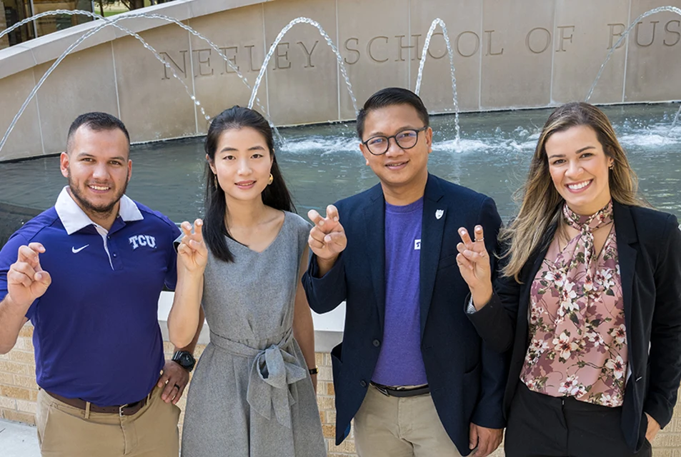 Four Neeley students make the Go Frogs sign in front of the Neeley fountain