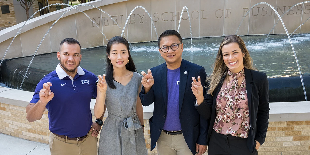 Four Neeley students make the Go Frogs sign in front of the Neeley fountain