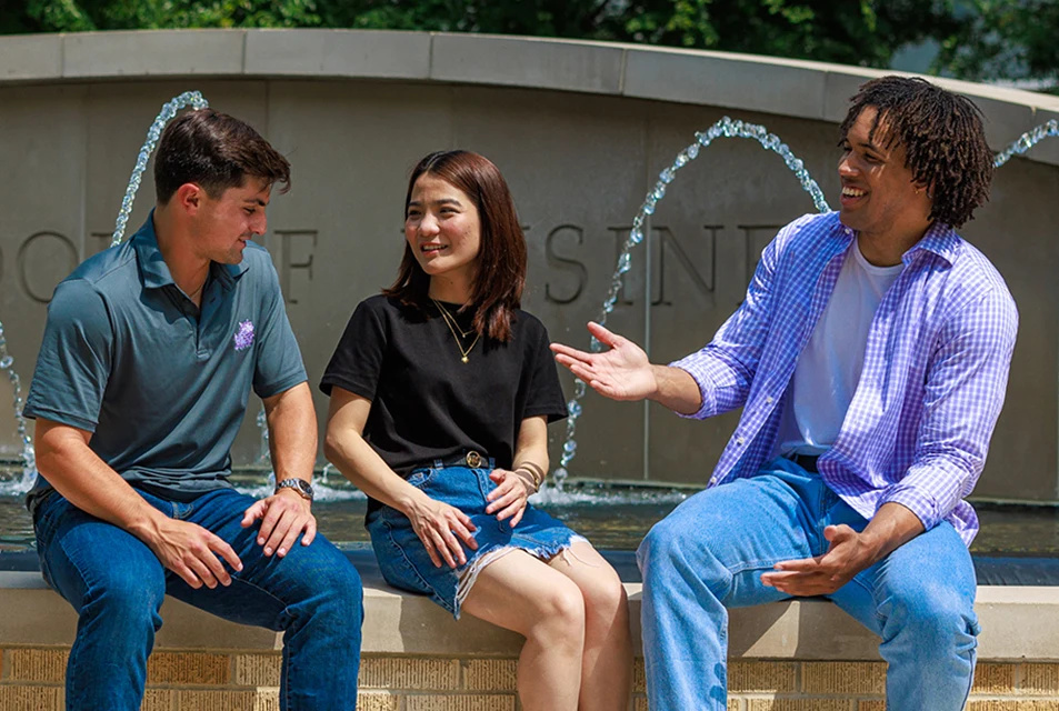 Three students sit on the edge of the Neeley fountain and chat