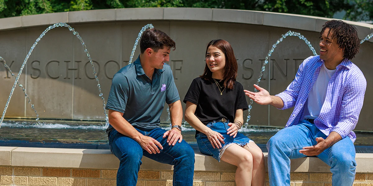 Three students sit on the edge of the Neeley fountain and chat