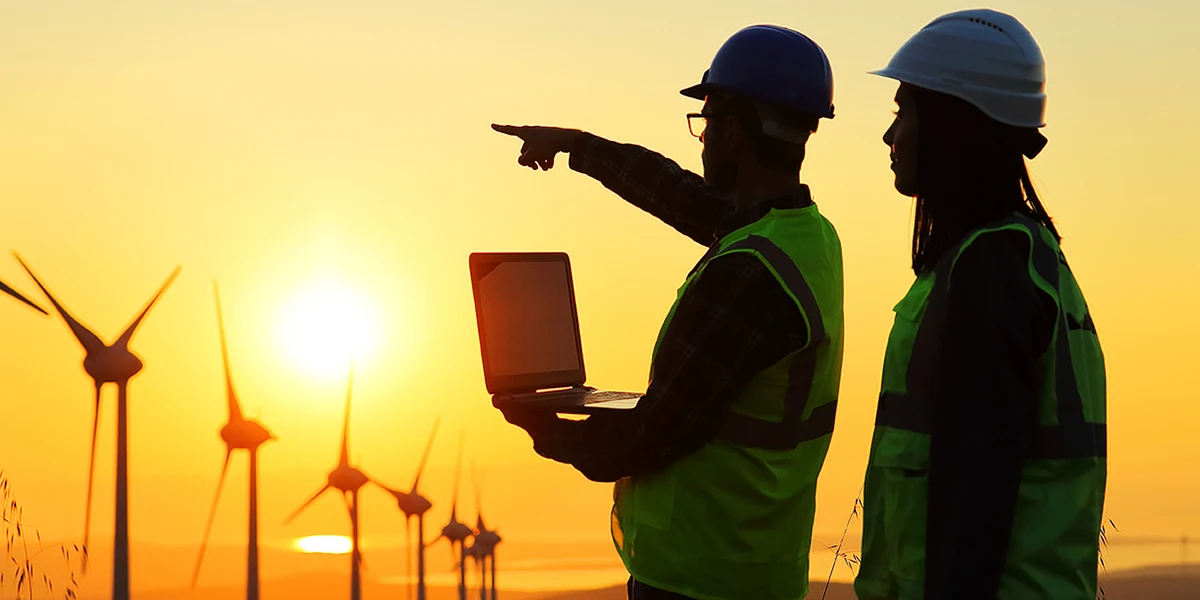 An instructor gestures toward a line of wind turbine generators while working with a student on-site