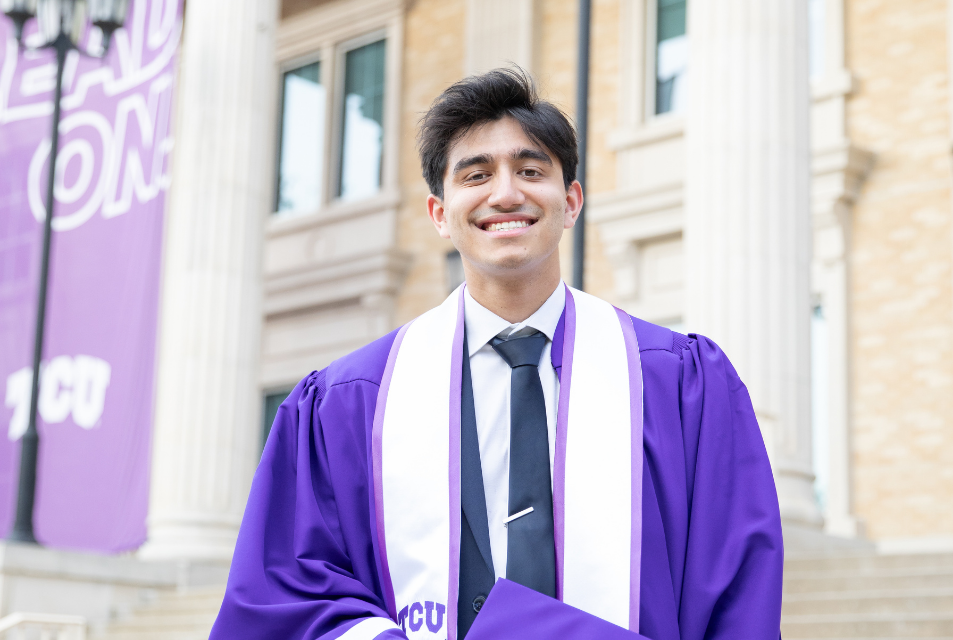Student in graduation regalia in front of  library. 