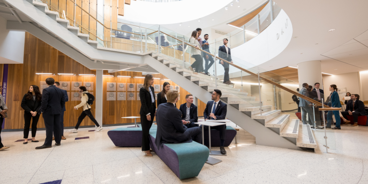 Clusters of students standing and walking at the base of the stairs in Dan Rogers Rotunda in the Neeley School of  Business.